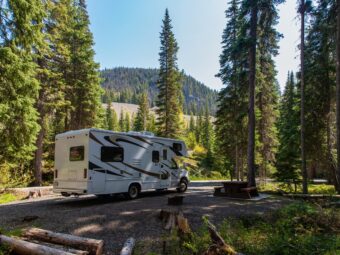 Beautiful campsite in the mountains with an RV and wooden bench.